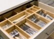 Open kitchen drawer with a wooden organizer holding neatly arranged forks, knives, spoons, and other silverware.