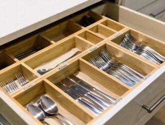 Open kitchen drawer with a wooden organizer holding neatly arranged forks, knives, spoons, and other silverware.