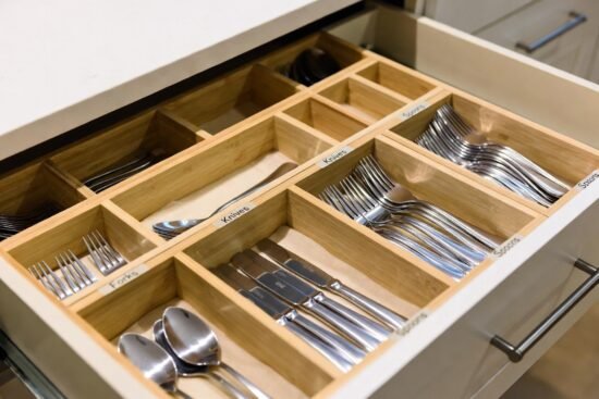 Open kitchen drawer with a wooden organizer holding neatly arranged forks, knives, spoons, and other silverware.