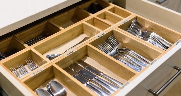 Open kitchen drawer with a wooden organizer holding neatly arranged forks, knives, spoons, and other silverware.
