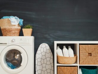 Organized small laundry closet with floating wooden shelves and clear detergent jars above stacked machines