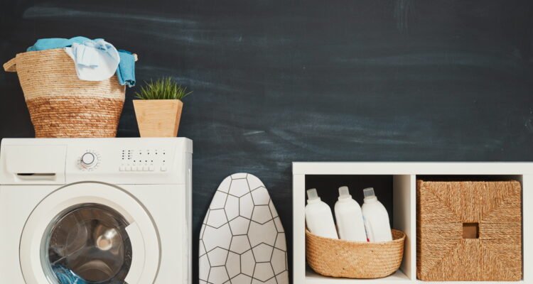 Organized small laundry closet with floating wooden shelves and clear detergent jars above stacked machines