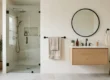 Bright bathroom with a black towel bar by the shower door, a folded bath towel and a hand towel ring near the mirror